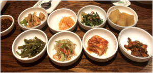 Eight plain white ceramic bowls containing a variety of colorful banchan.