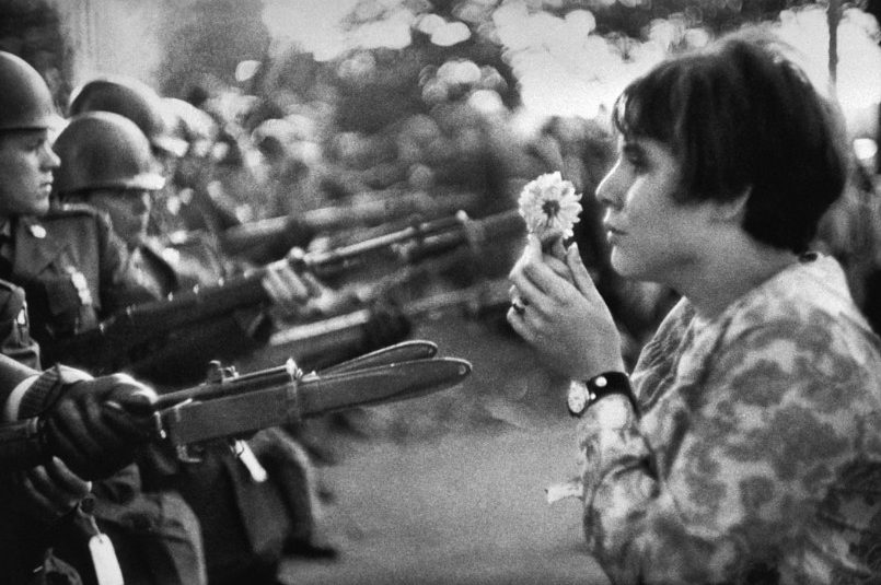 a woman holds a flower in front of armed men